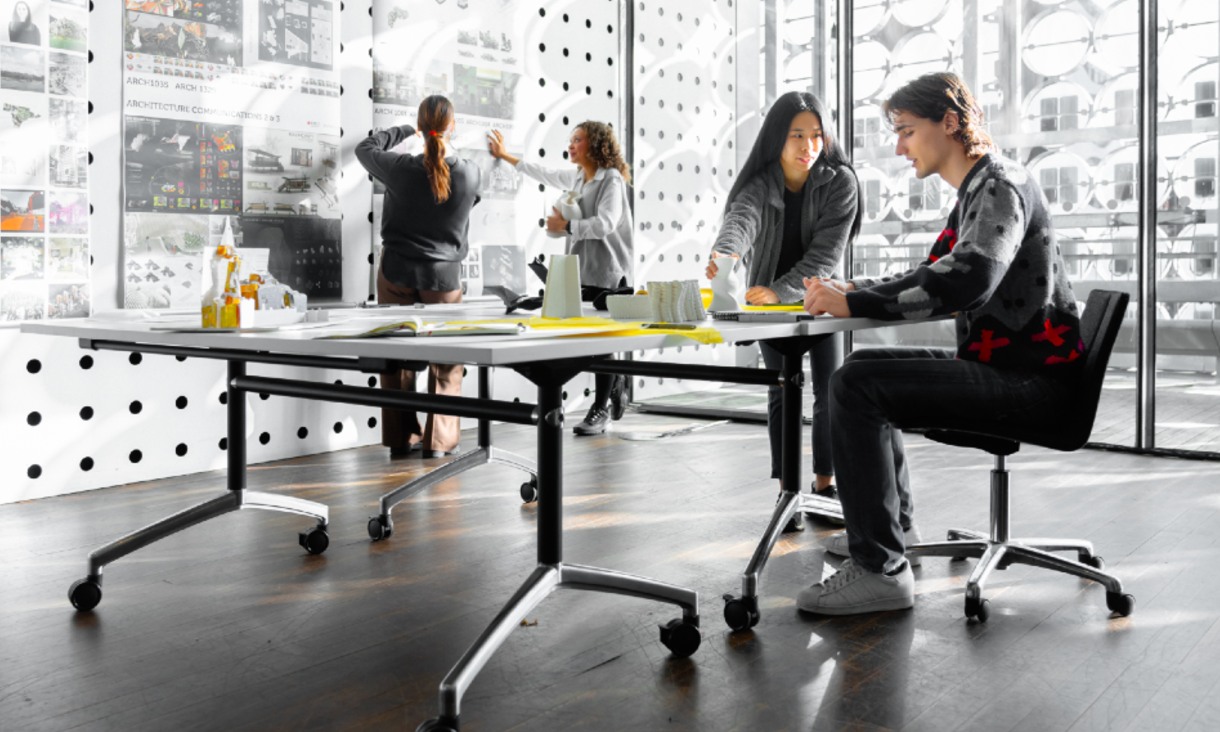 A group of people collaborating and discussing architectural designs pinned on a wall. 