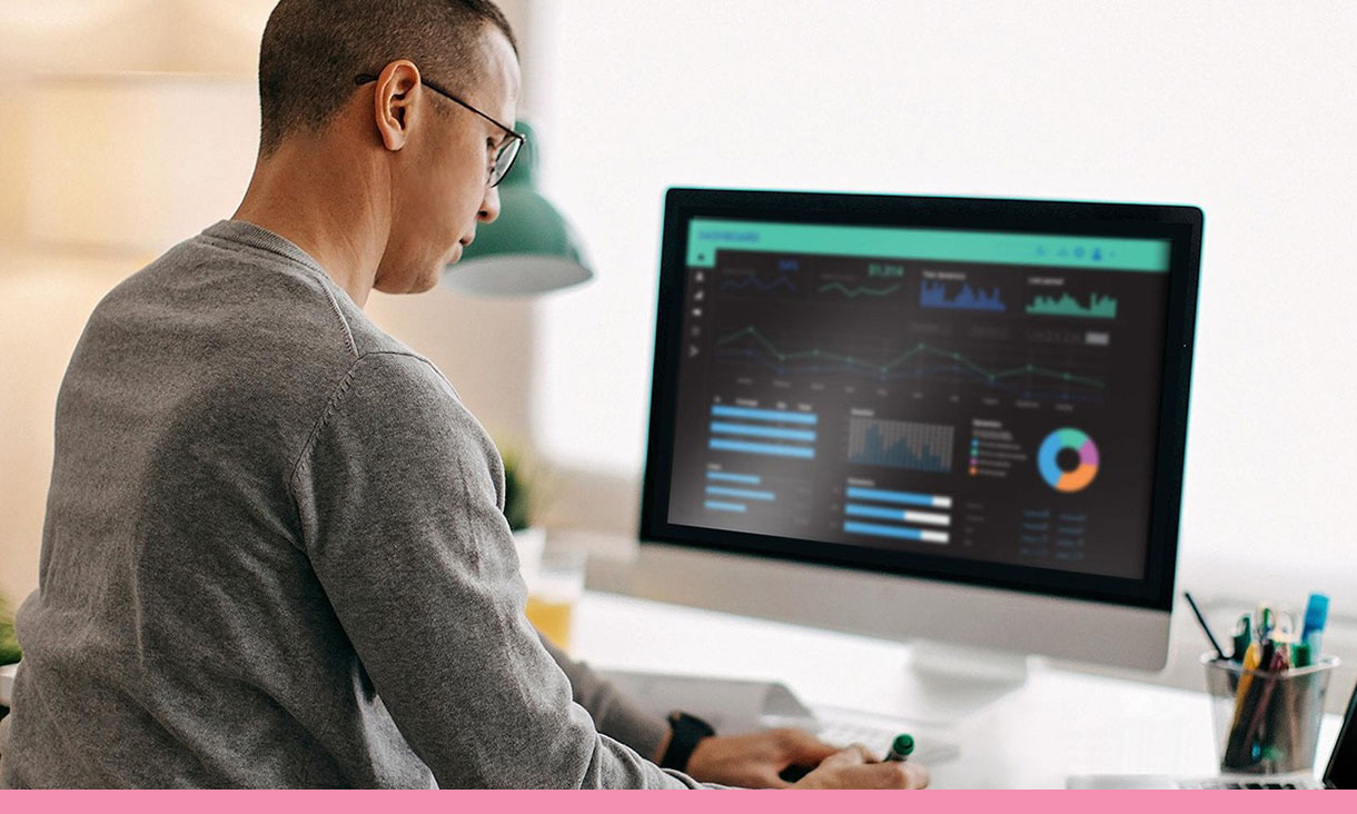 A man takes notes from his computer which displays data and tables.
