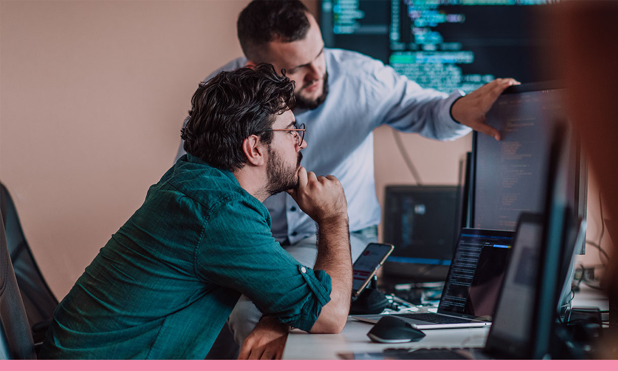 Two coworkers look at and discuss computer code.