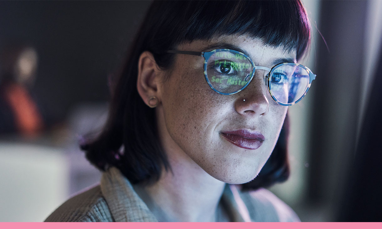 Portrait of a woman, computer code is reflected in her glasses.