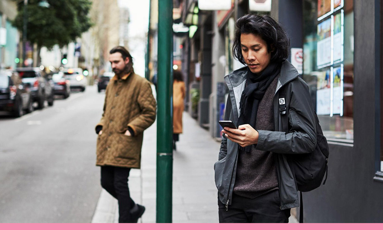 A man checks his phone while standing on a street corner.