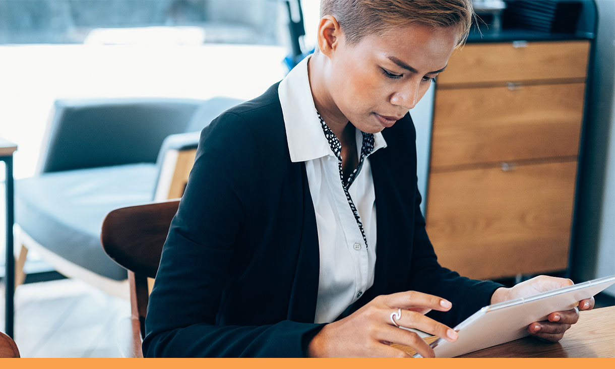 A person sits at a table and looks at a tablet.