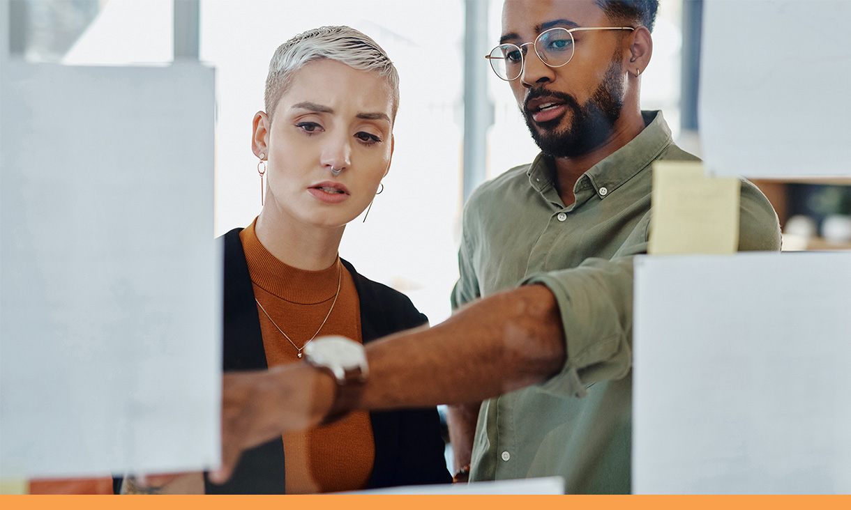A man points to a computer screen in discussion with his coworker.