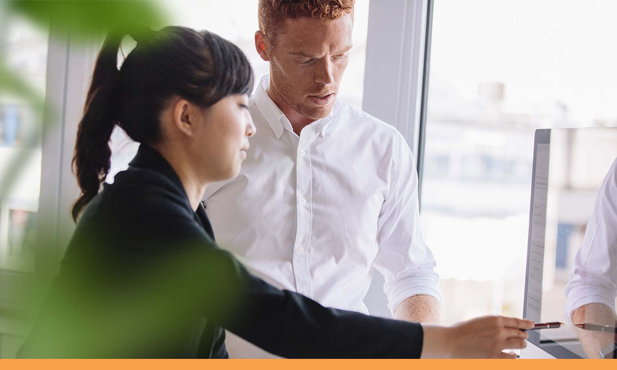 A woman points to a computer screen in discussion with her coworker.