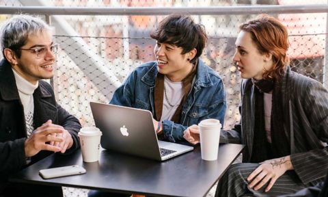 Three students sitting at a table with coffee cups and a laptop.