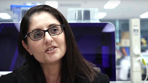  Mary Tolcos, in front of large computer screen, talking to camera