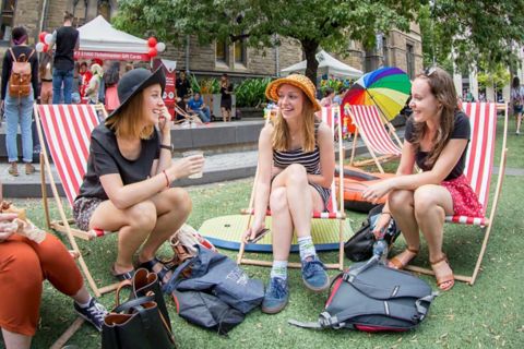 Three women sit on deck chairs and laugh together on campus.