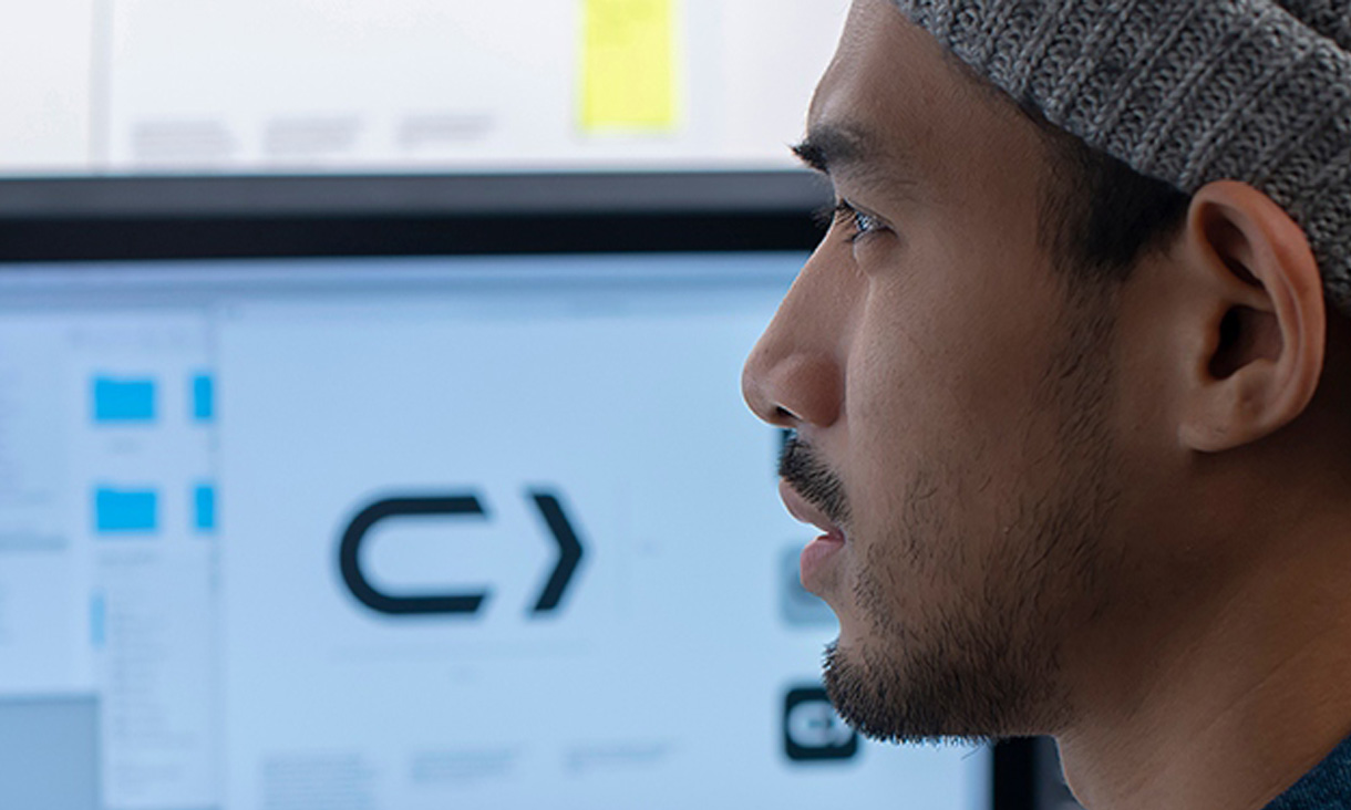 A man sits in front of a computer working an some logo designs. 