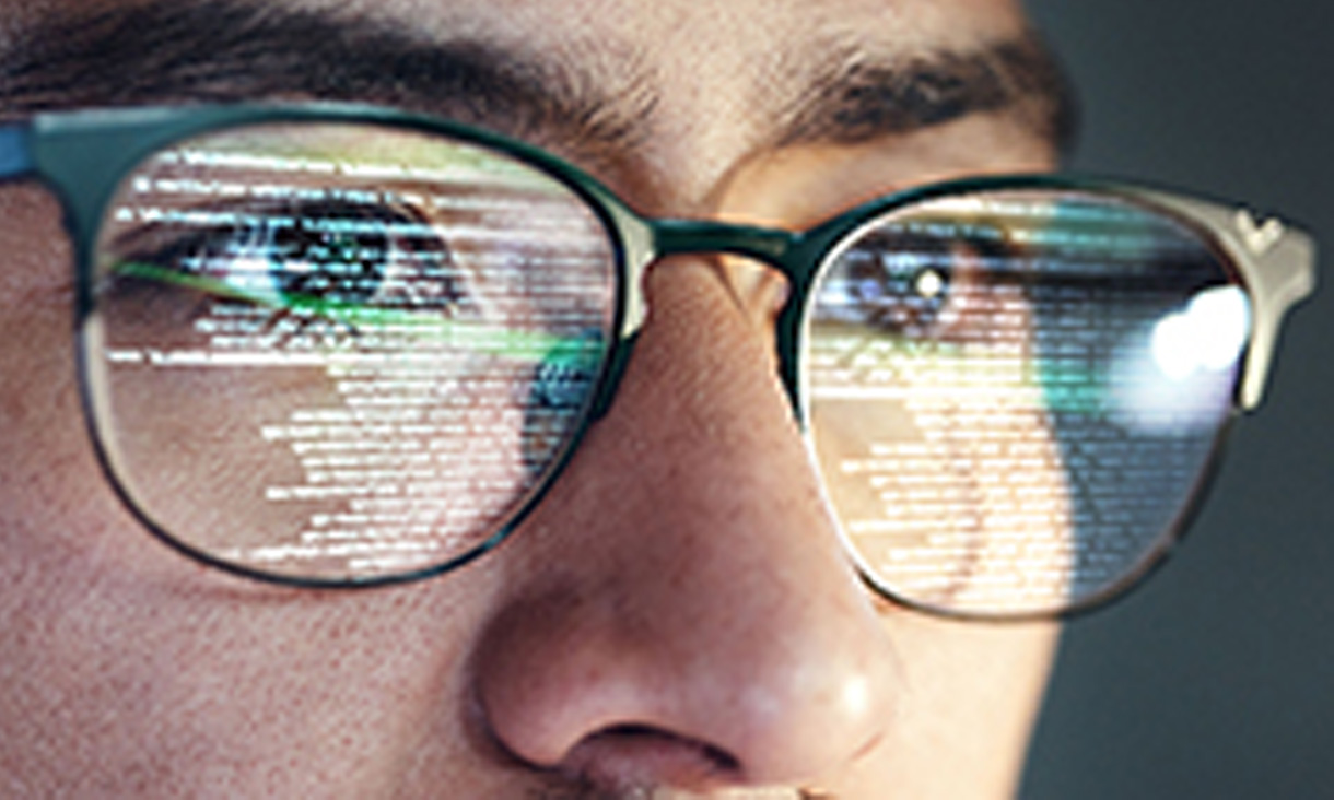 A man in glasses with code reflecting off the lenses. 