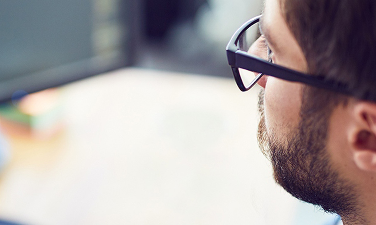 A man in glasses looking at two computer that he is writing code on. 