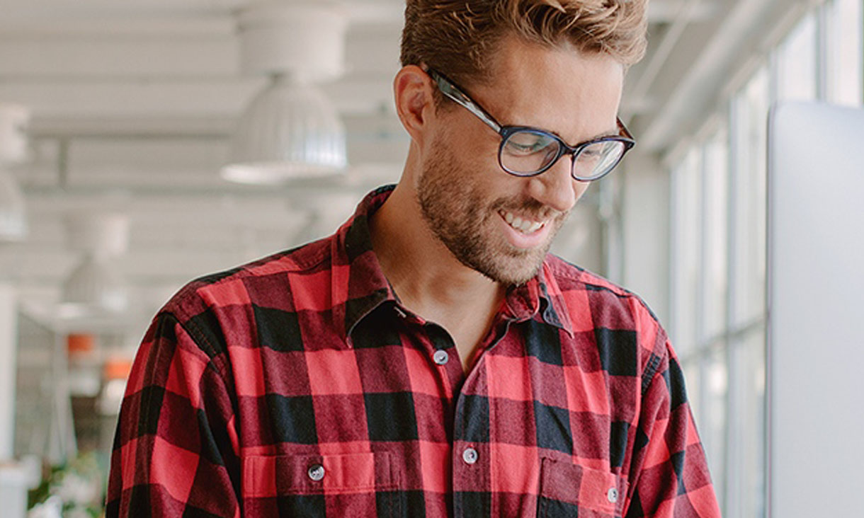 A man in glasses sits at his computer in an office.