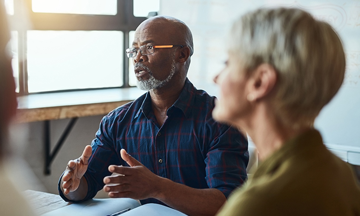 A man talks in a meeting with others.