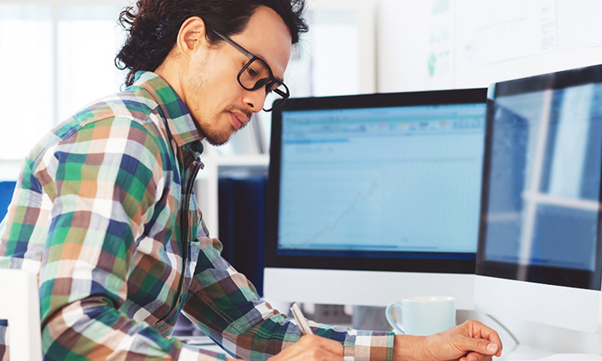 A man sits at his desk in an office and writes a note.