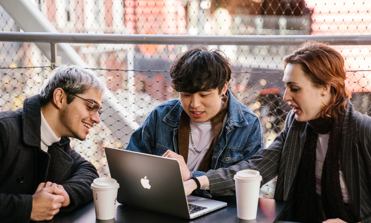students seated around table facing laptop while smiling in discussion